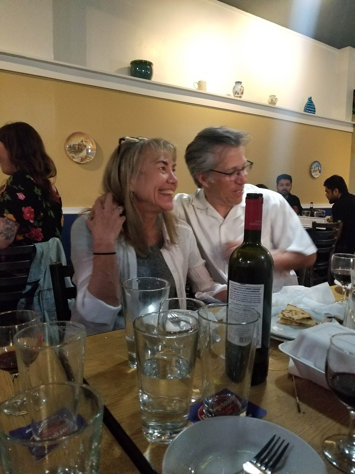 My mom, Cindy, and dad, Dan, sitting in a restaurant, with water glasses and a wine bottle on the table. This is my mom's favorite restaurant, Taki's Mad Greek in Seattle, Washington.