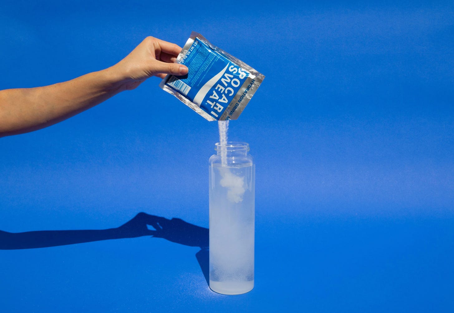 A sachet of Pocari Sweat electrolyte powder being mixed into a bottle of water, preparing a hydration drink. A sachet of Pocari Sweat electrolyte powder being mixed into a bottle of water, preparing a hydration drink.