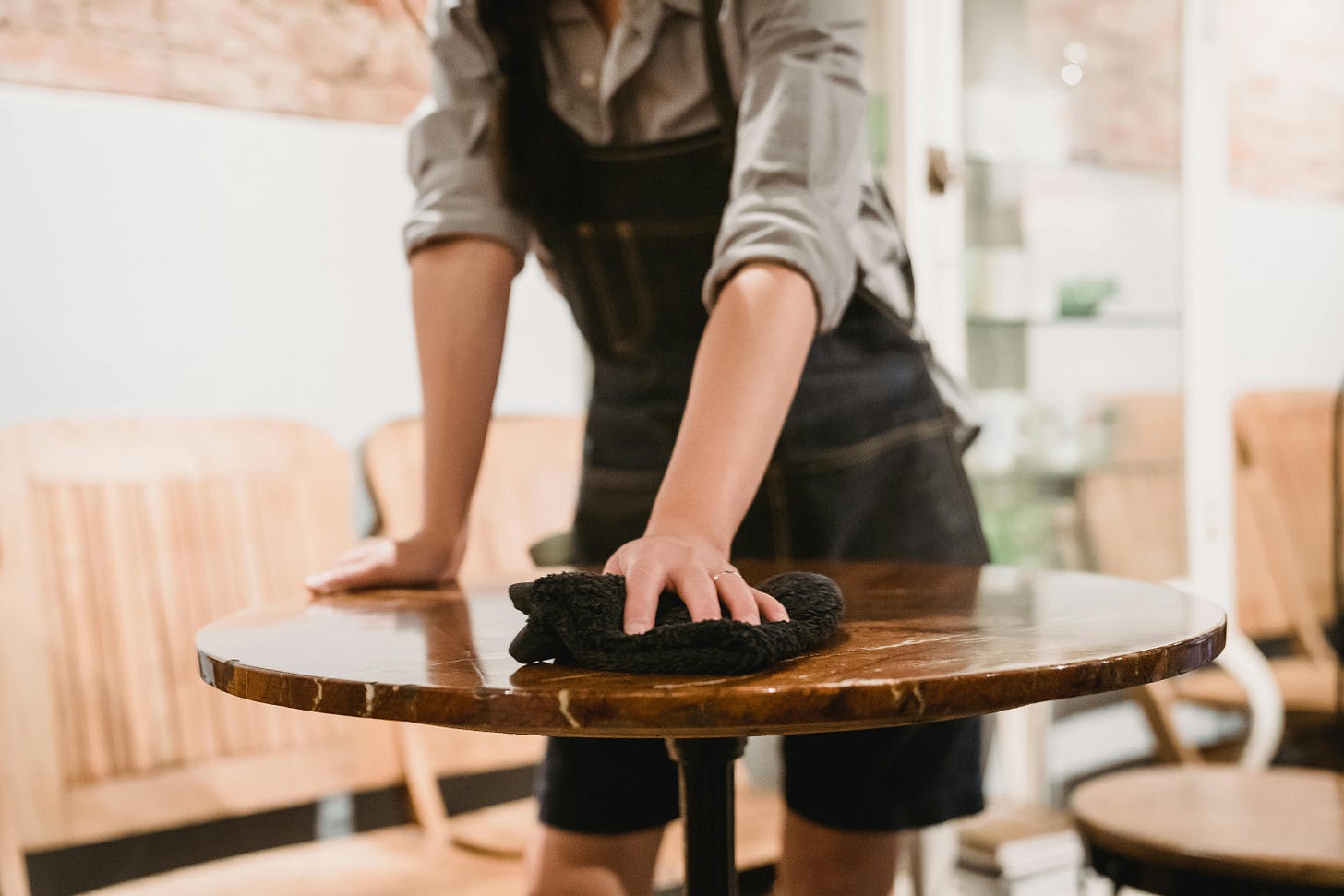 A photo of a person wearing overalls wiping down a cafe table indoors