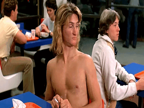 a shirtless man sits at a table in a fast food establishment