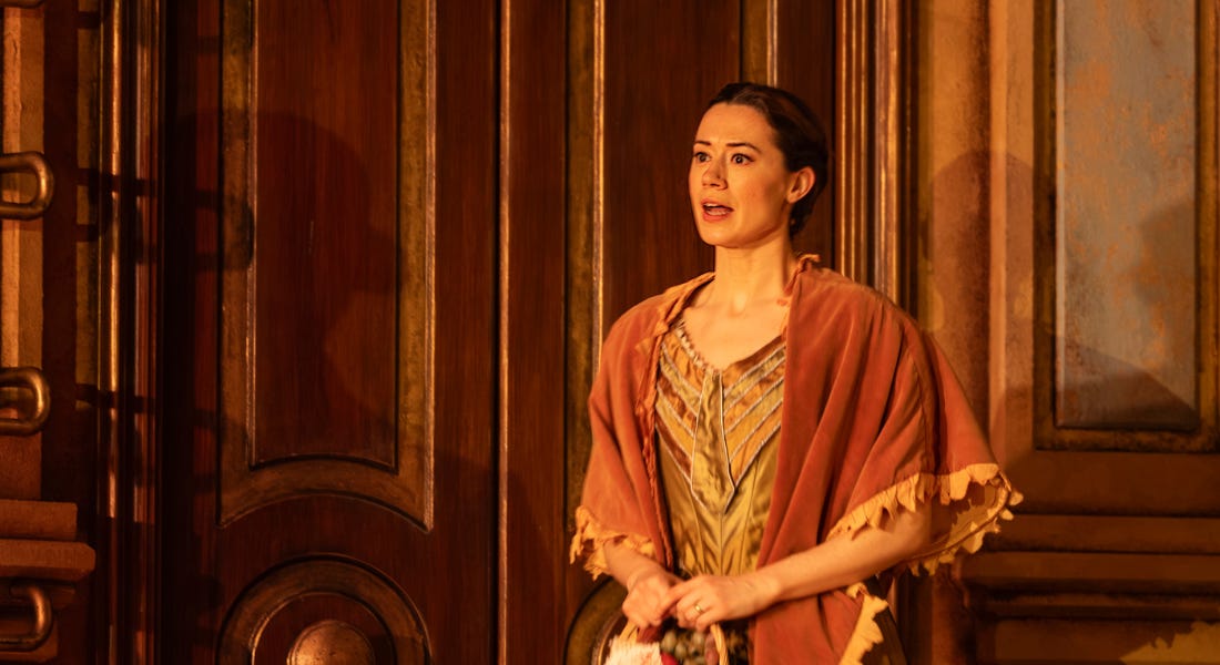 A woman with black hair wearing a dress and a shawl standing in front of a brown wooden door A woman with black hair wearing a dress and a shawl standing in front of a brown wooden door