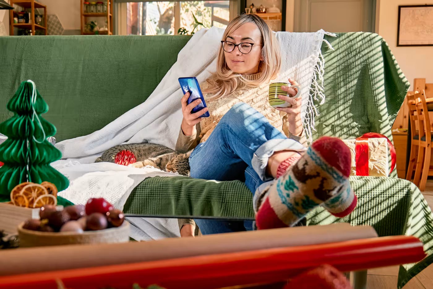 A person sitting on a couch holding a phone and a mug

Description automatically generated
