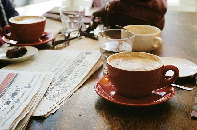 This may contain: two cups of coffee sit on a table next to newspapers and other items in front of them