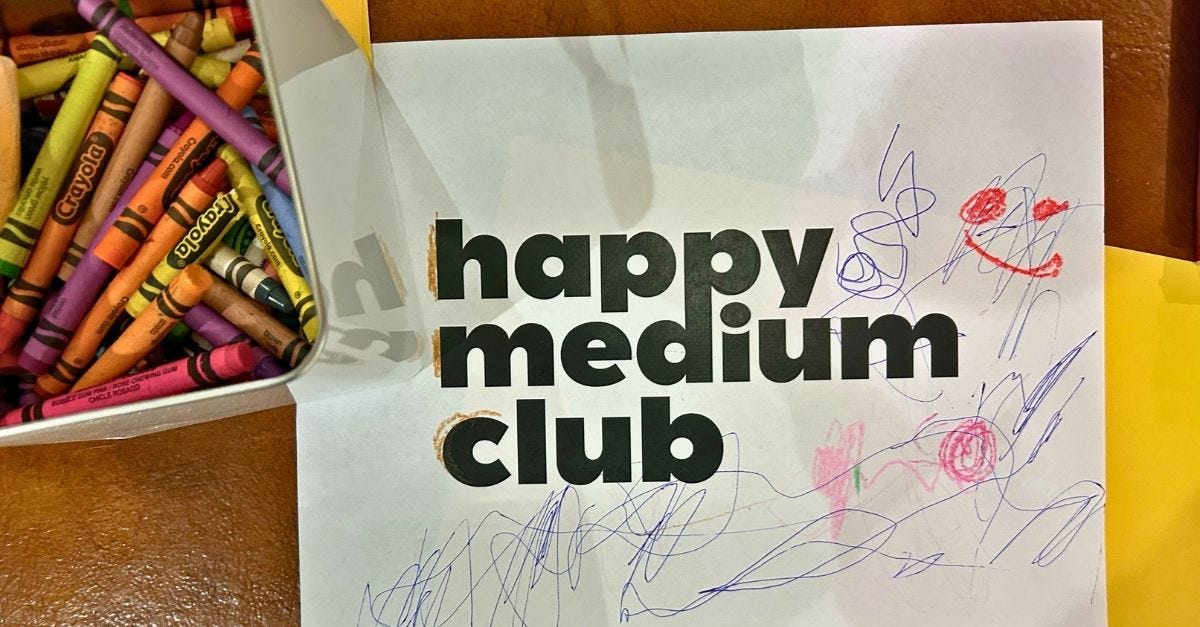 A piece of paper with the Happy Medium Club logo covered in crayon scribbles. 