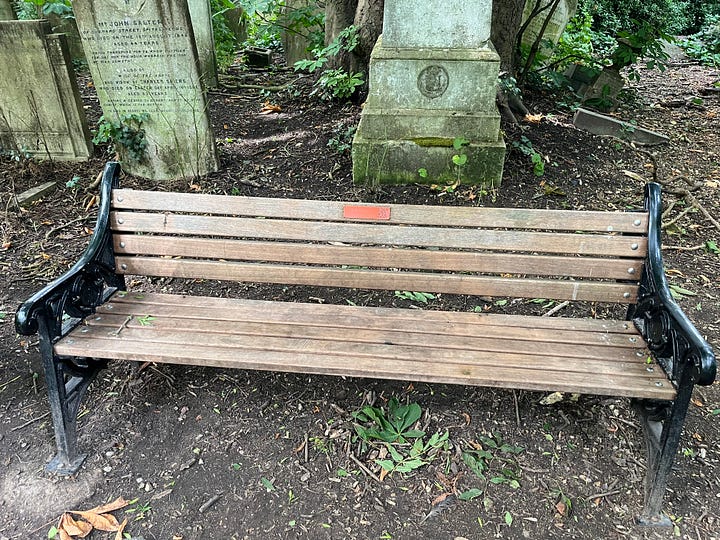 A bench with a bright orange label reading “Mark Bridgeford - A man you don’t meet every day.” with a QR code
