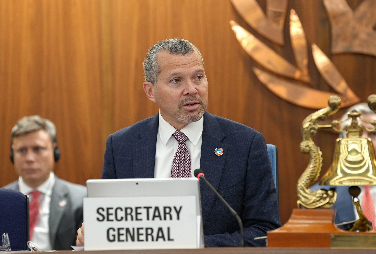 IMO Secretary-General Arsenio Dominguez speaks during the 76th session of the IMO Technical Cooperation Committee at IMO Headquarters, seated behind a "Secretary General" nameplate in a wood-paneled conference chamber.