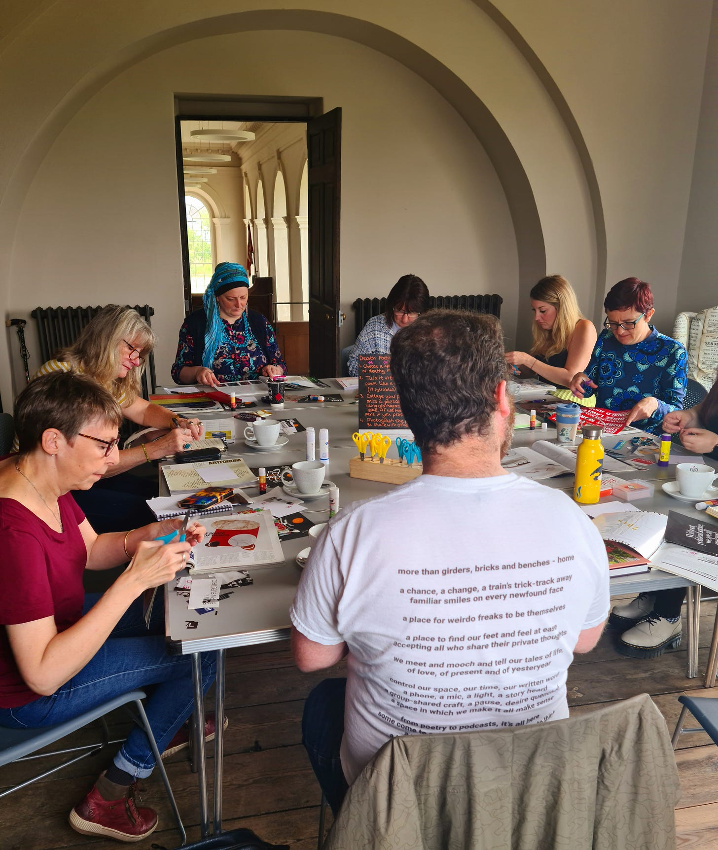A group of eight adults sat at a table collaging deathy haikus onto blank postcards.