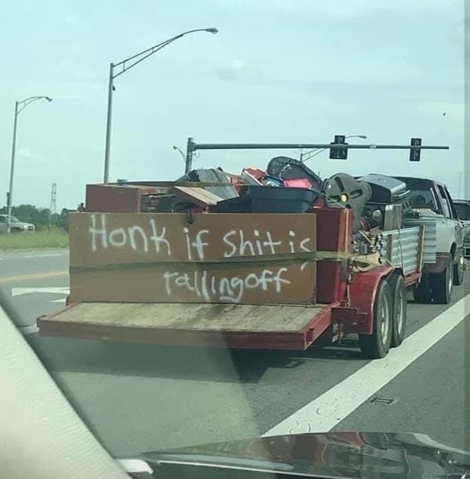 A photo of a loaded trailer with a hand-painted sign on the back reading "Honk if shit is falling off."