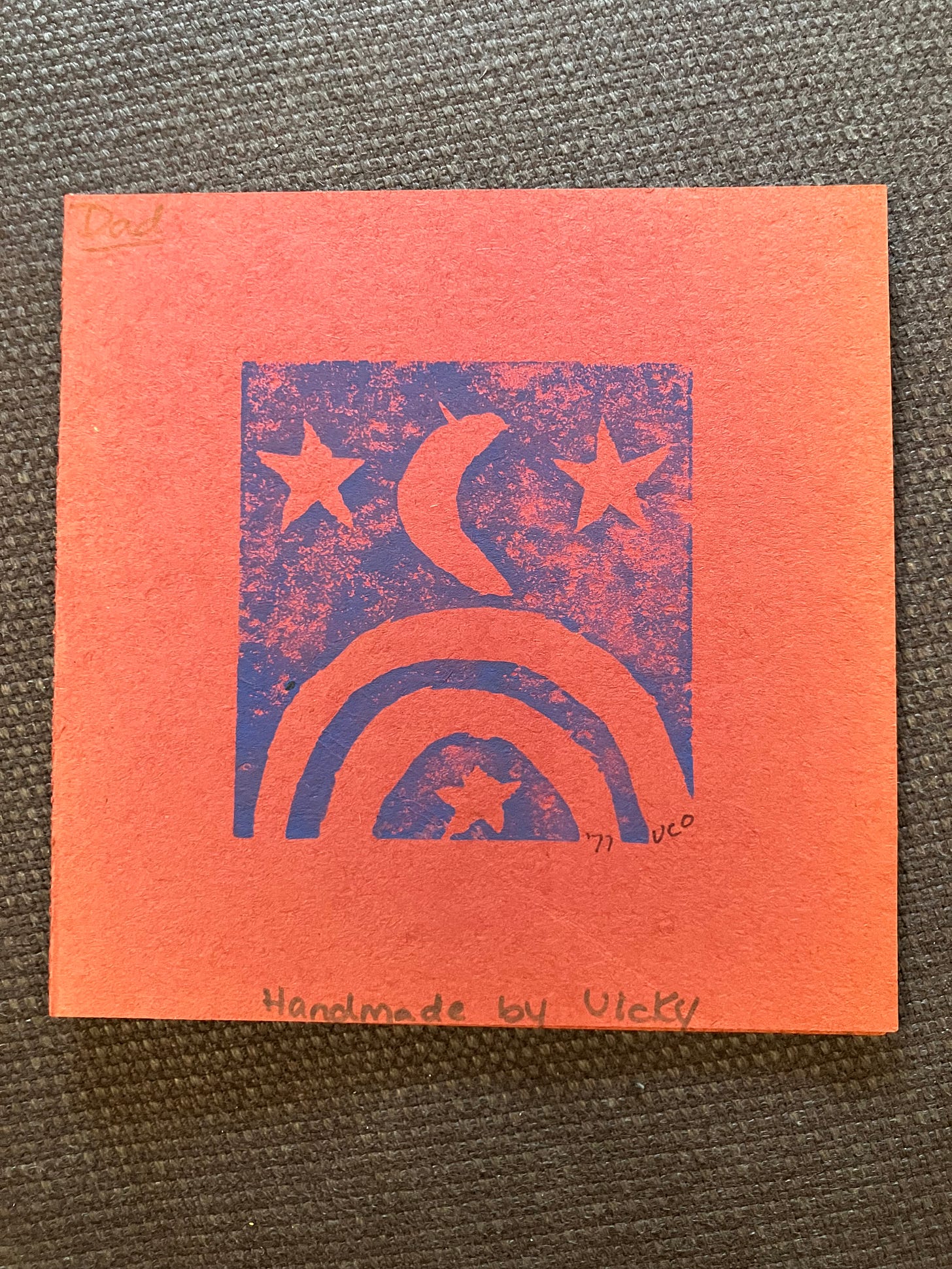 a handmade card on reddish paper with a dark blue woodcut of stars, crescent moon, and rainbow, signed to Dad, VCO '71.