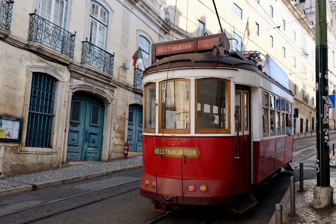A red and white, old-fashioned tram heading downhill in a historic district of Lisbon, Portugal
