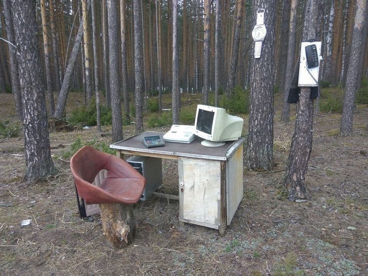 This may contain: an old desk in the woods with a chair and computer monitor on top of it