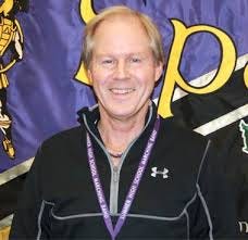 Portrait of veteran band director Joe Carl standing in front of a school band banner, smiling while wearing a black quarter-zip jacket and a purple lanyard with a medal. Carl has taught band at Sumner High School in Washington for more than three decades and is featured in an article about expertise, mentorship, and institutional knowledge in education. Portrait of veteran band director Joe Carl standing in front of a school band banner, smiling while wearing a black quarter-zip jacket and a purple lanyard with a medal. Carl has taught band at Sumner High School in Washington for more than three decades and is featured in an article about expertise, mentorship, and institutional knowledge in education.