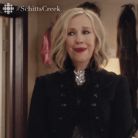 Moira from TV's Schitts Creek looks at the camera. The subtitles say "Colour me curious"