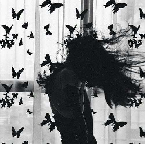 Mujer cerca de una ventana con mariposas negras volando a su alrededor Mujer cerca de una ventana con mariposas negras volando a su alrededor