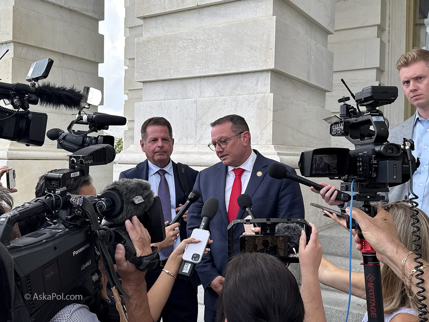 Cameras record as microphones wave in faces of two men in suits Photo: Matt Laslo © AskaPol.com