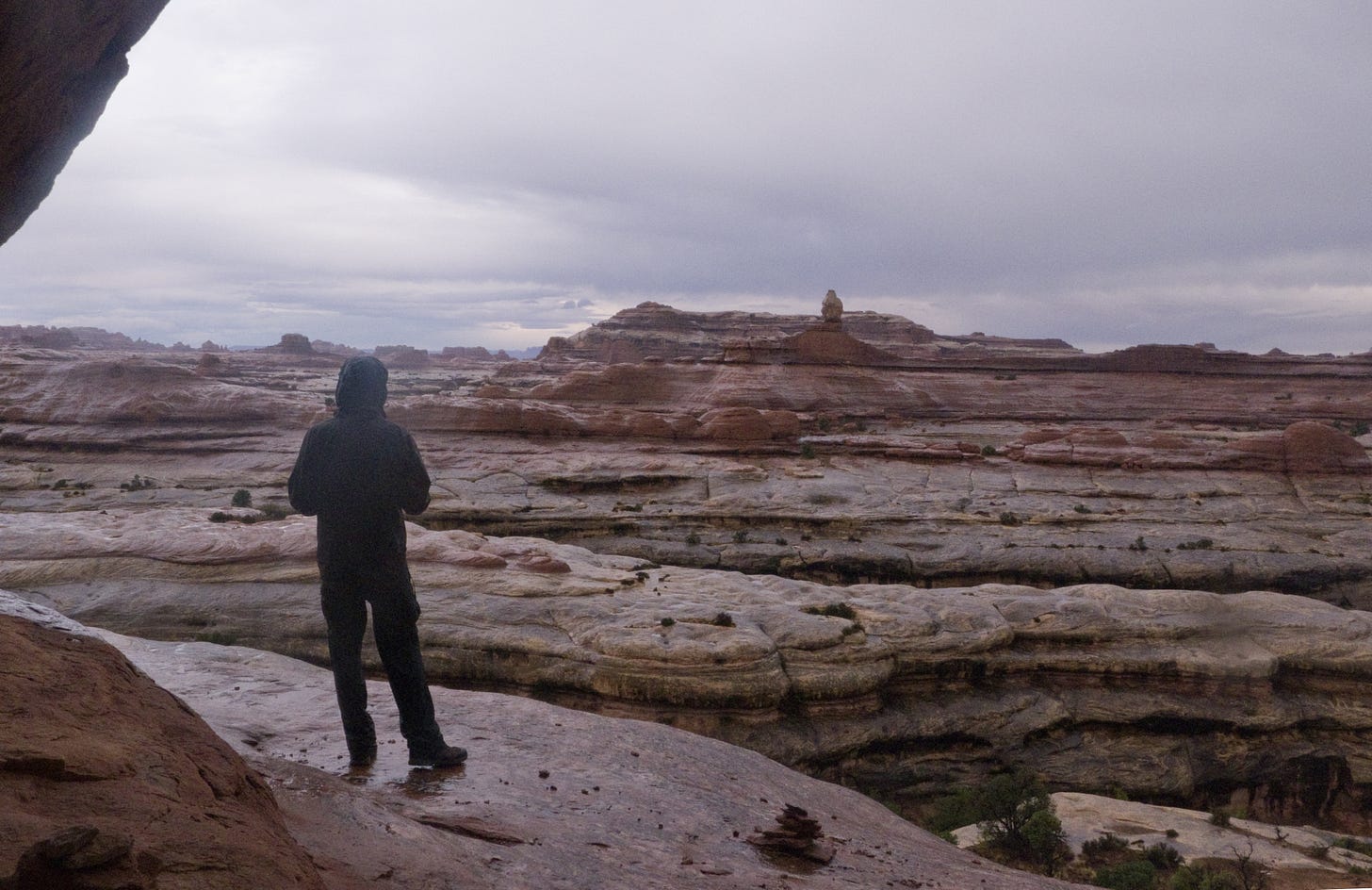 person on expanse of wet sandstone, with clouds and rock towers