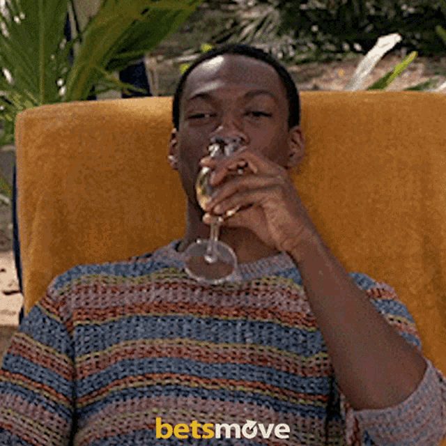 a man in a striped sweater sits in a chair holding a glass of wine ..