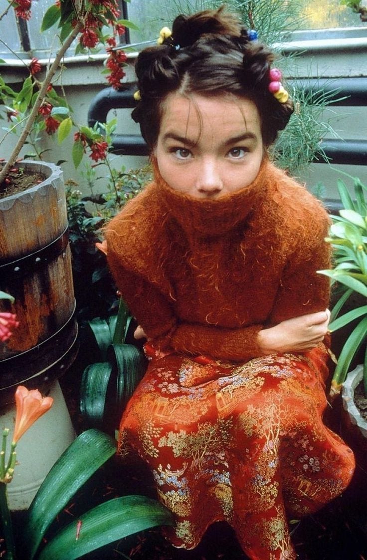 This may contain: a woman sitting on top of a bench next to potted plants and wearing a red dress