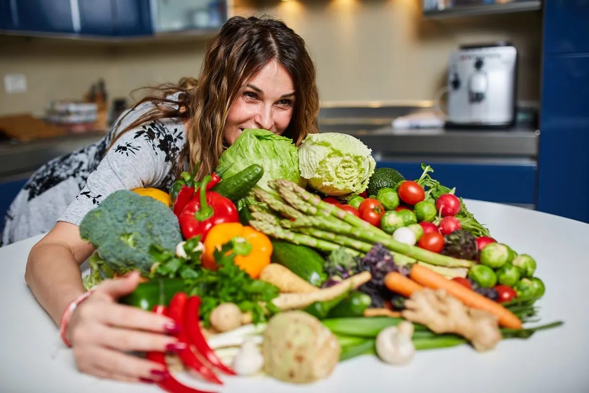 Smiling woman wraps her arms around a bountiful pile of fresh veggies on kitchen counter. Smiling woman wraps her arms around a bountiful pile of fresh veggies on kitchen counter.