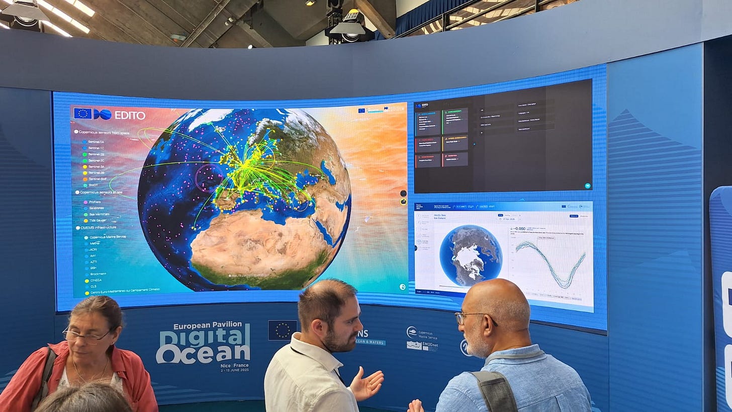 Foto. Estande com uma tela imensa mostrando o globo terrestre com foco na Europa, com várias linhas saindo da europa, mostrando os sistemas de observação do oceano e satélites deles