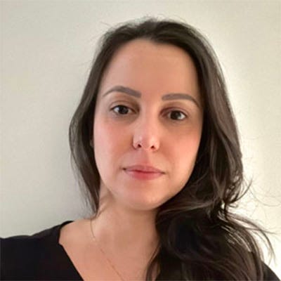 Mulher de cabelos compridos e olhos negros, usando blusa preta e colar com pingente no pescoço