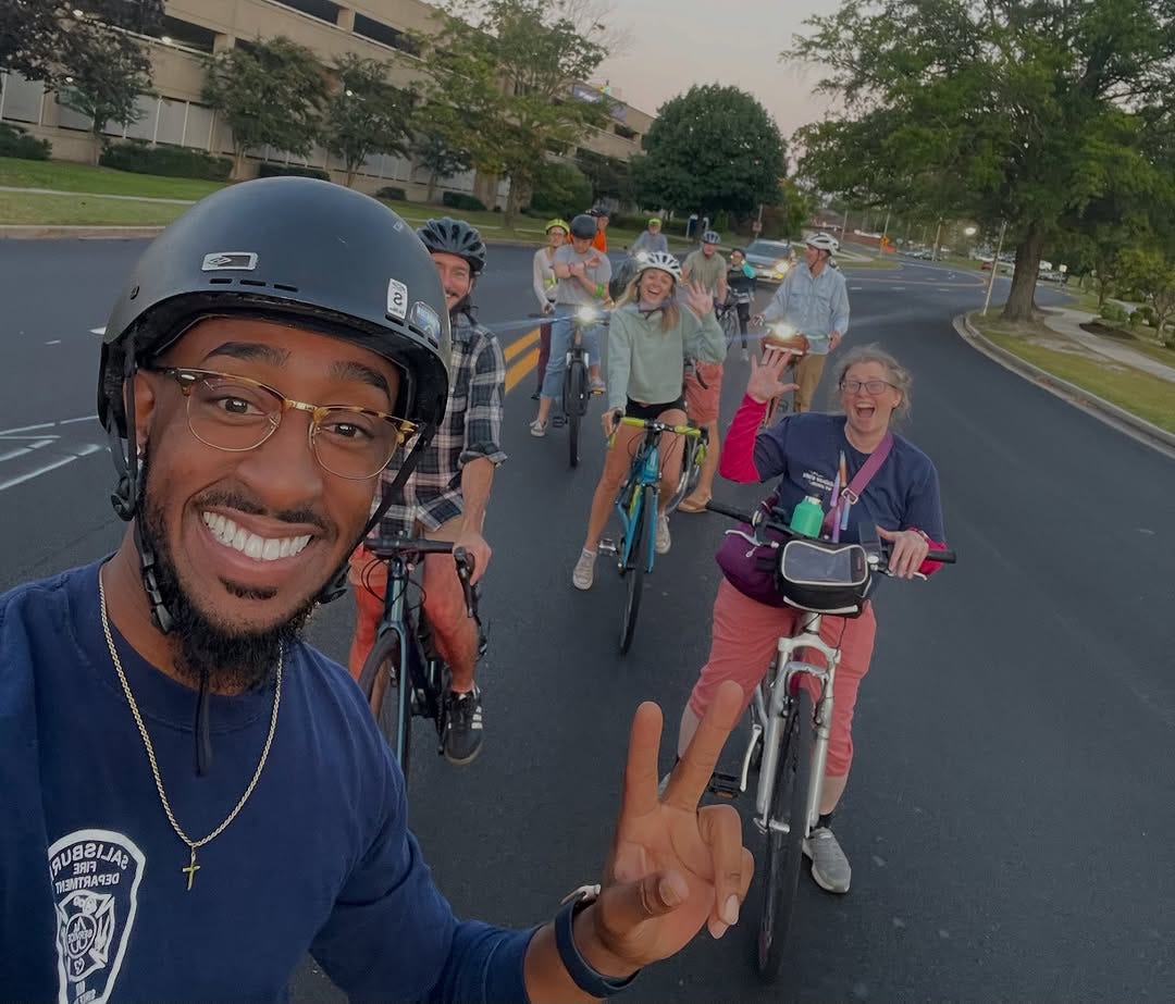 Doughty rides his bike, flashing the peace sign to constituents during a community event.