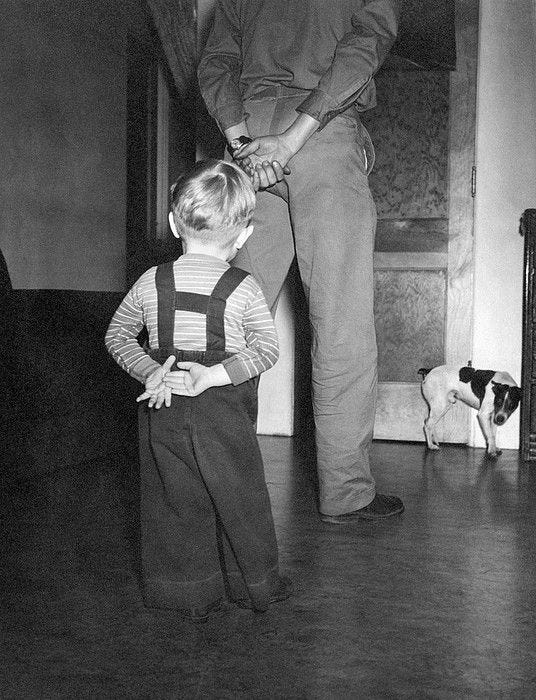 This may contain: an old black and white photo of a little boy standing in front of his father