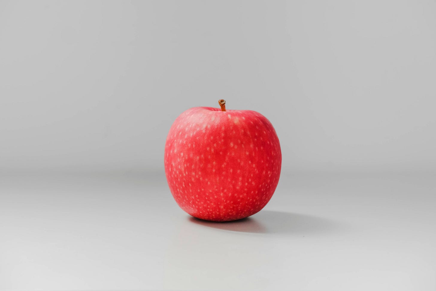 Shiny red apple on gray background, resembling Newton's famous inspiration for gravity, perfect symbol for personal branding myths article