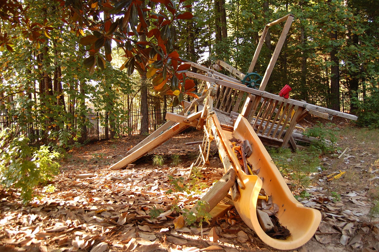 A wooden swingset, half-collapsed and surrounded by trees