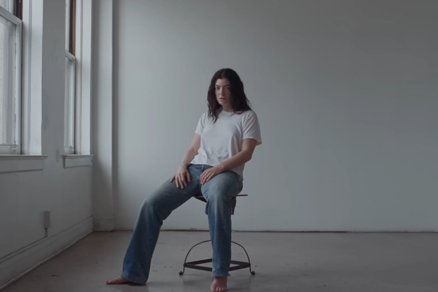 Lorde sits on a chair in a stark bare room