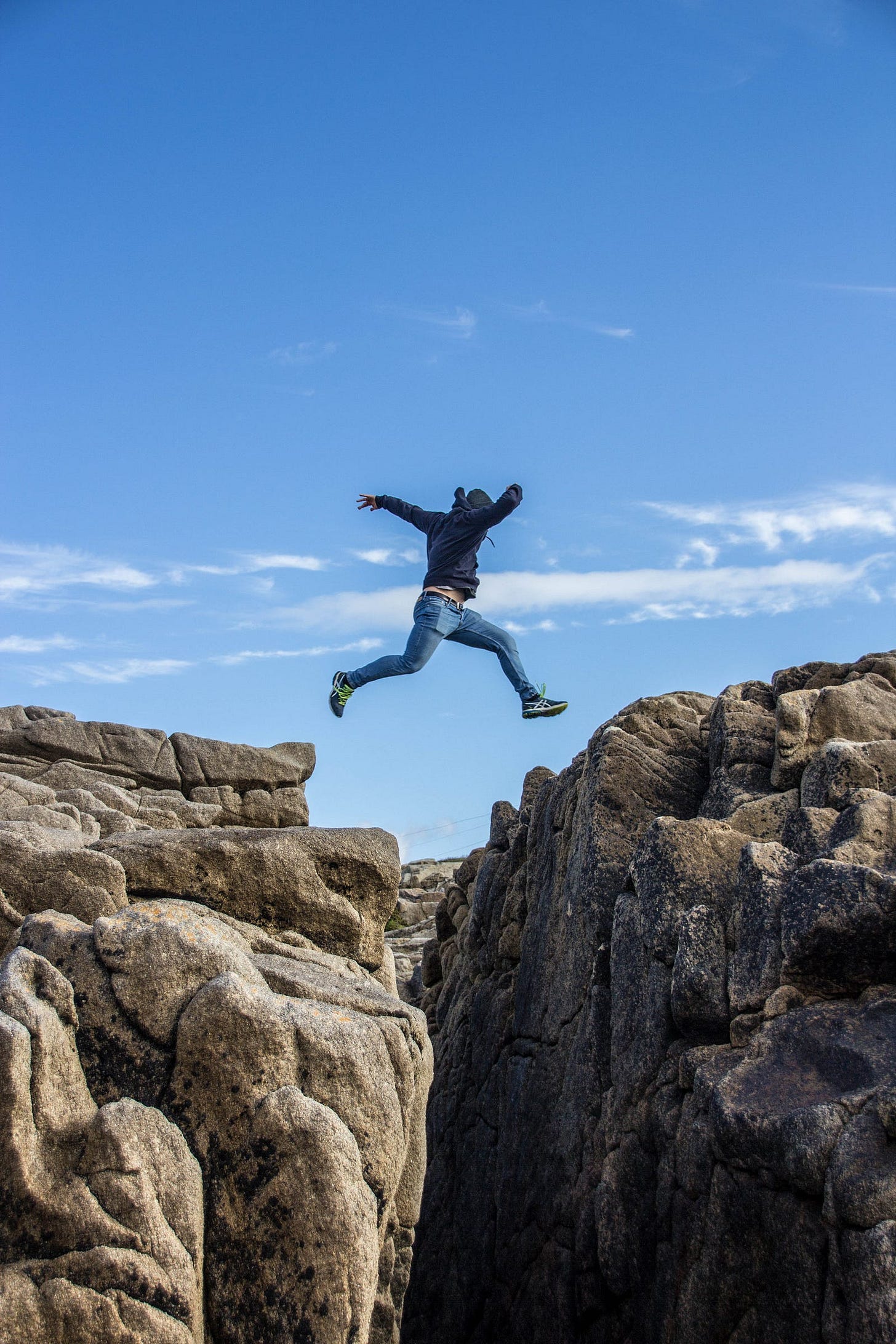 man in black jacket and blue jeans jumping on brown rocks during daytime