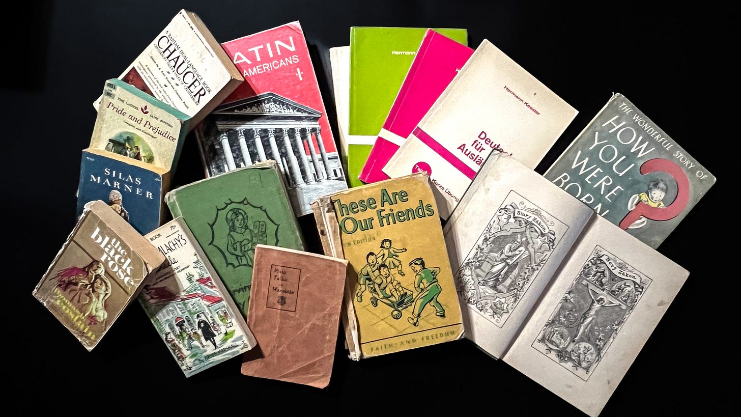Old books layed out on a black background, novels, Latin and Gerrman textbooks, early readers and catechism booms from 1907 to 1950s, a marriage couseling book from the 1940s and a How You were Born from the early 1950s