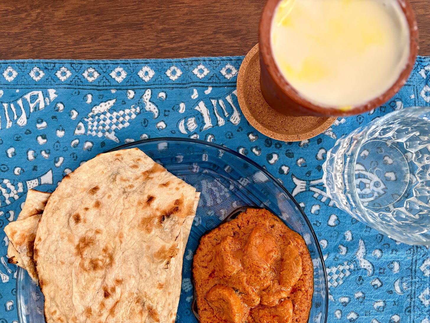 Plate of butter chicken with naan and a glass of lassi, showing a classic introduction to Indian cuisine.