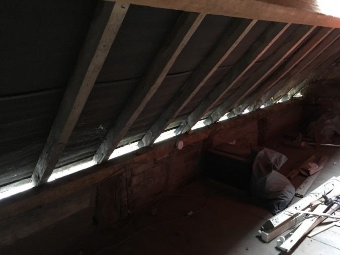 A sloping attic roof with beams and a strip of daylight coming in where the soffit is missing