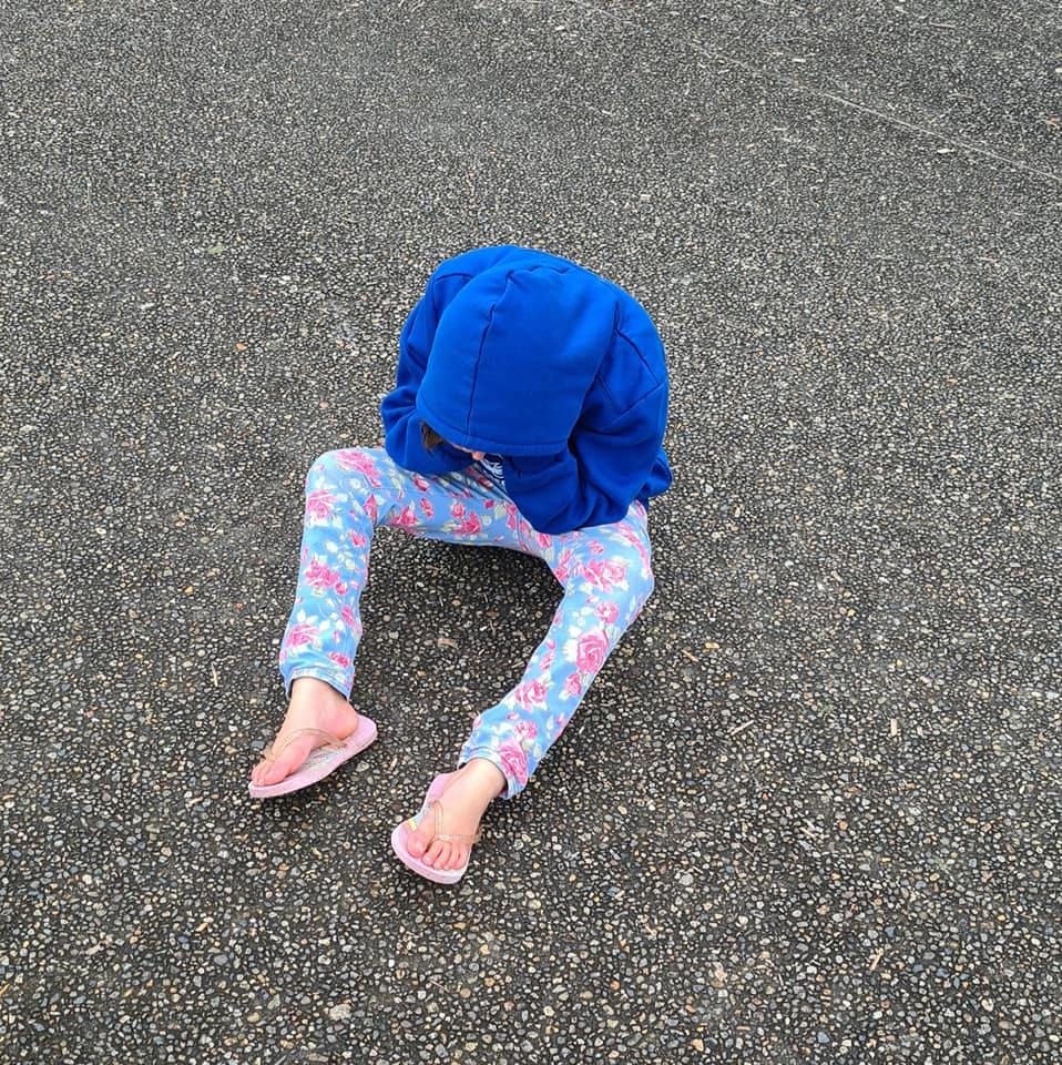 a young child in a blue hoodie sits on the ground, their head in their hands