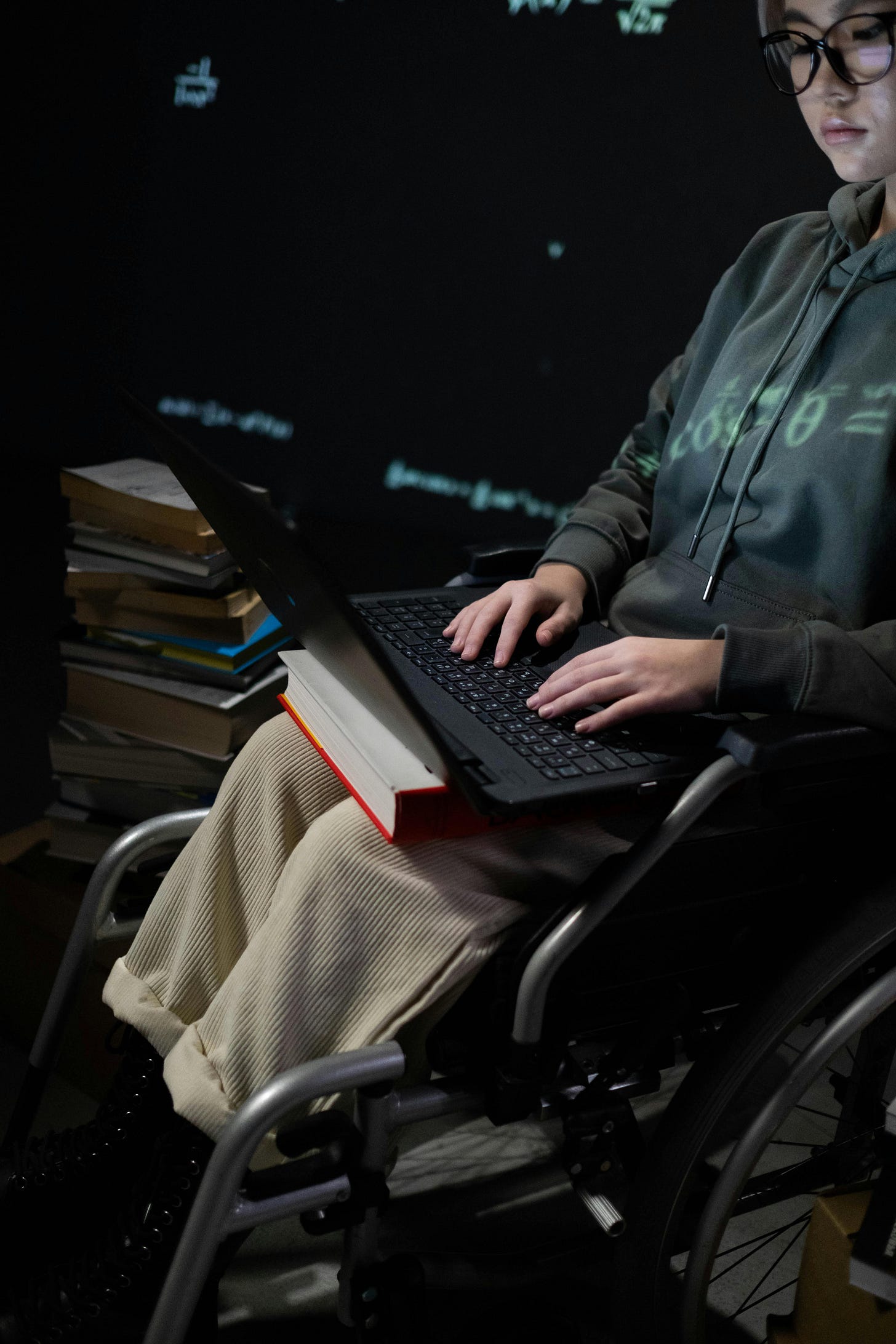 A girl sitting in her wheelchair typing on a laptop next to books A girl sitting in her wheelchair typing on a laptop next to books