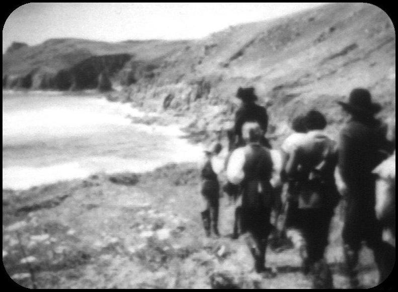 A monochrome photograph taken from a television screen showing a small group of men in 17th century dress, one on horseback, looking towards a coastal bay from a position approaching a clifftop. 