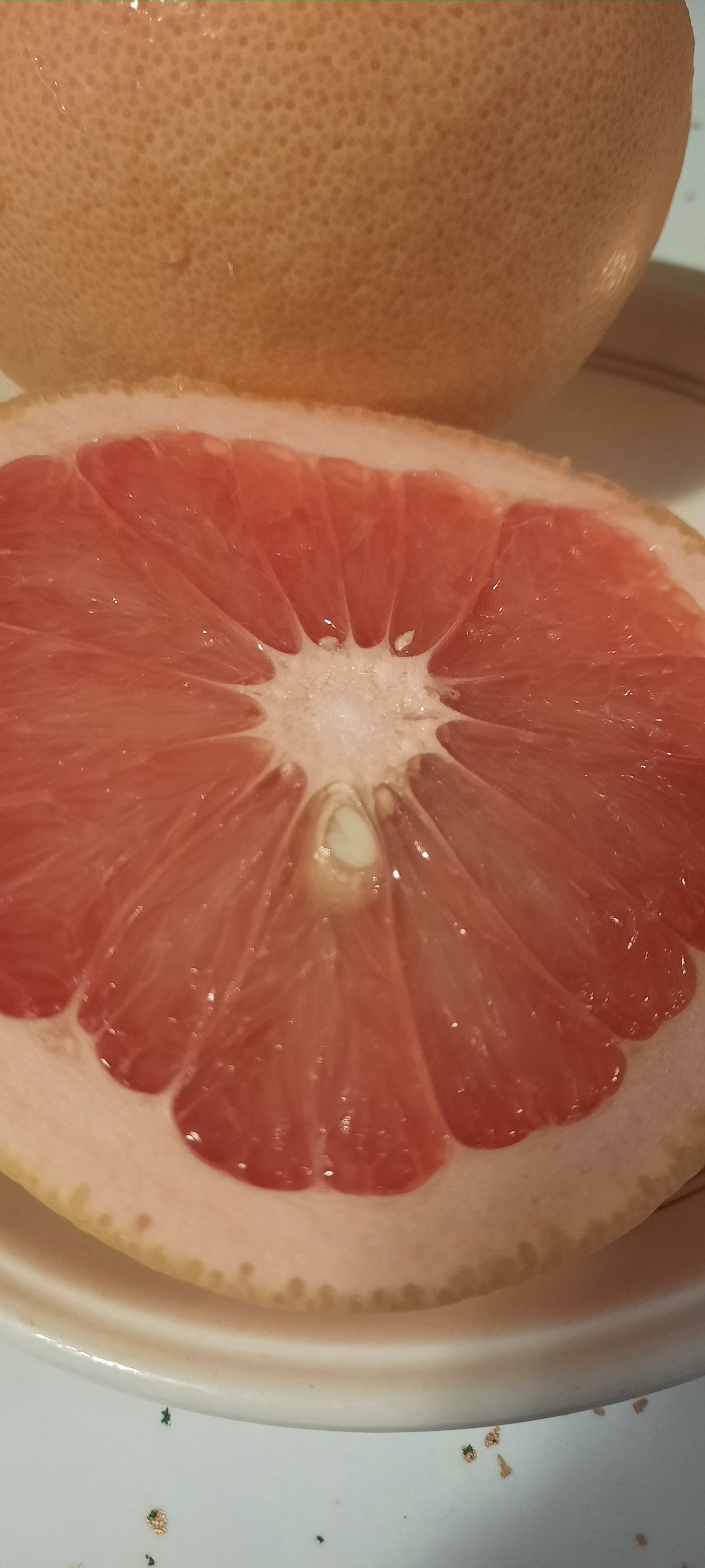 Half a grapefruit showing the pink inside. Behind is a yellow-pink whole grapefruit