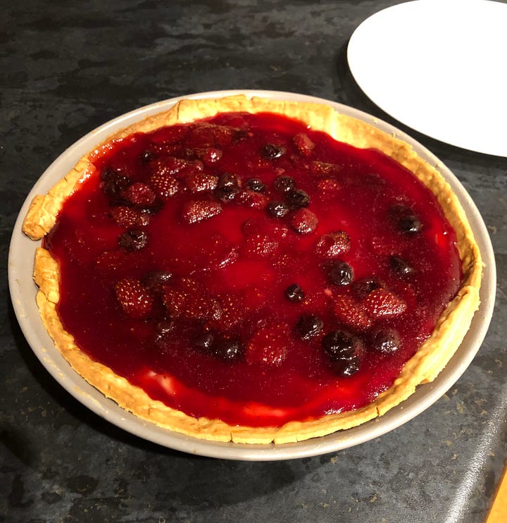 A bowl of strawberries, pastry on floor, a fruit flan