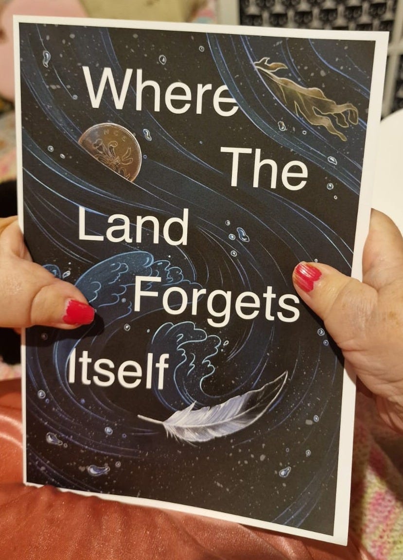 Penny’s small hands hold a poetry pamphlet. Cover reads where the land forgets itself in large white bold font. The cover is a blur of images in large swirls of dark blues, thin white lines delineating waves, a seagull feather in white grey and black curving in the right corner. On the left underneath the word there is a coin, and on the top right is a small frond of brown seaweed.