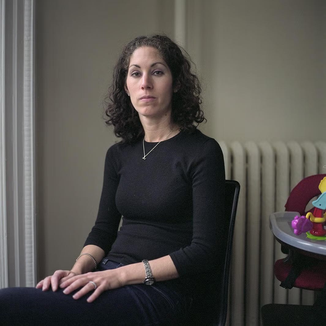 woman with serious expression, shoulder length dark hair, black blouse; off to side is a high chair with a toy on it  woman with serious expression, shoulder length dark hair, black blouse; off to side is a high chair with a toy on it