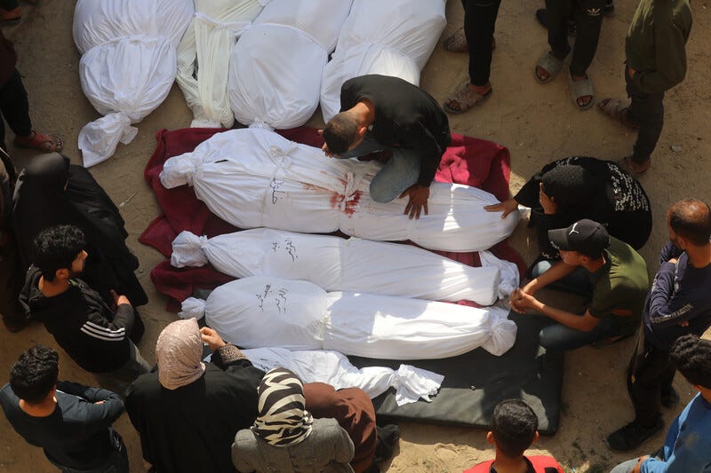 Overhead view of men and women sitting next to several shrouded bodies