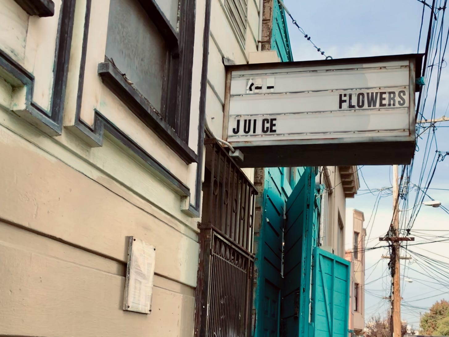 A marquee sign on a sunny city street advertising both juice and flowers