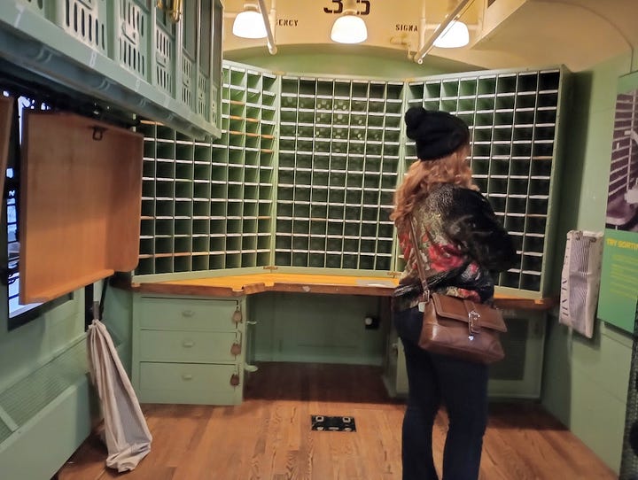 Photo of man in early 20th century sorting mail on train, mailbags and slots on mail train carriage in museum. Mail catcher used by moving train
