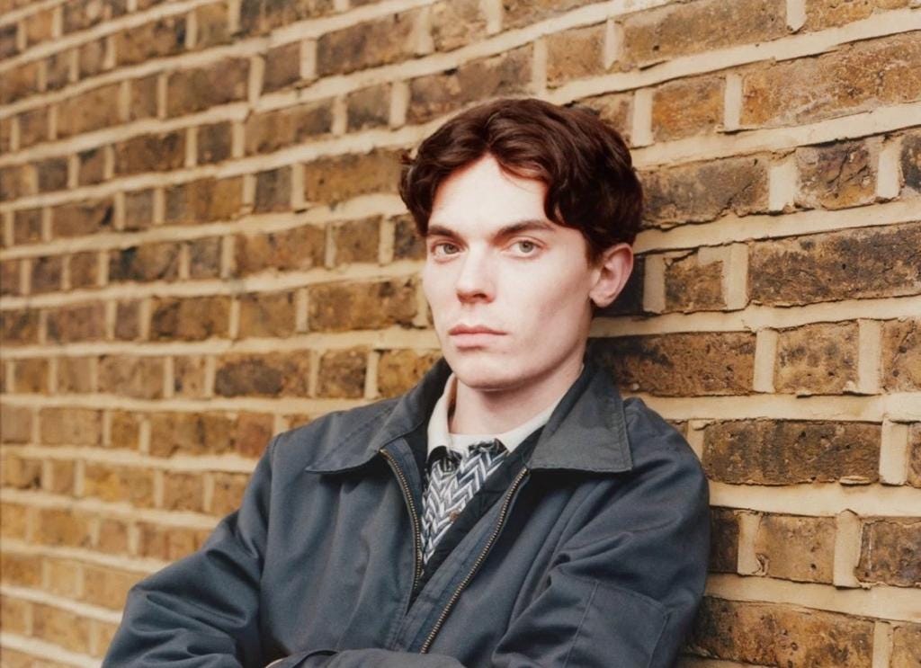 A person leaning against a brick wall

Description automatically generated
