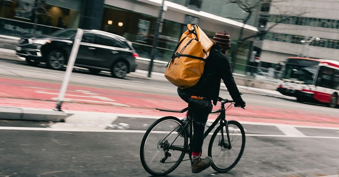 Cyclist with large yellow bag navigates city street