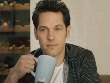 Paul Rudd in a polka dot shirt is holding a blue coffee mug