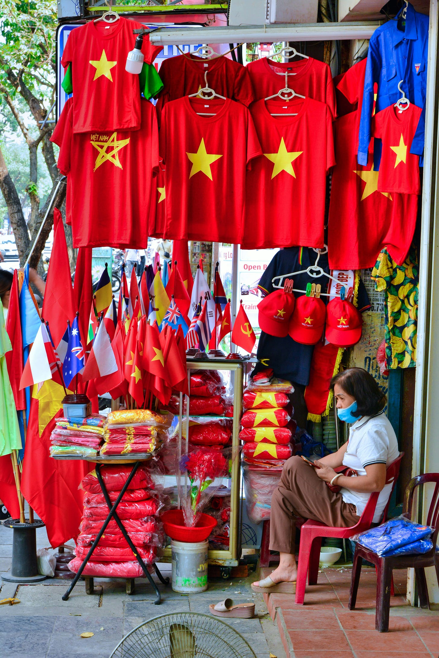 A vendor is tending to his stall selling Vietnamese-themed knick-knacks, including red T-shirts with a yellow star in the middle. A vendor is tending to his stall selling Vietnamese-themed knick-knacks, including red T-shirts with a yellow star in the middle.