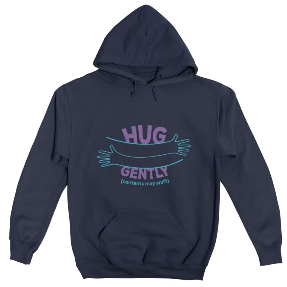Navy blue pullover hoodie featuring a teal and purple graphic of two arms wrapping around each other in a hug. Text reads, “HUG GENTLY (contents may shift).”