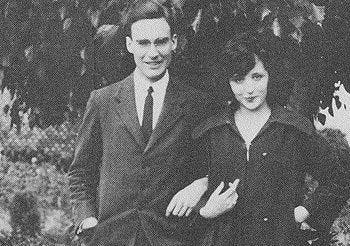 This may contain: an old black and white photo of two people standing next to each other in front of a tree